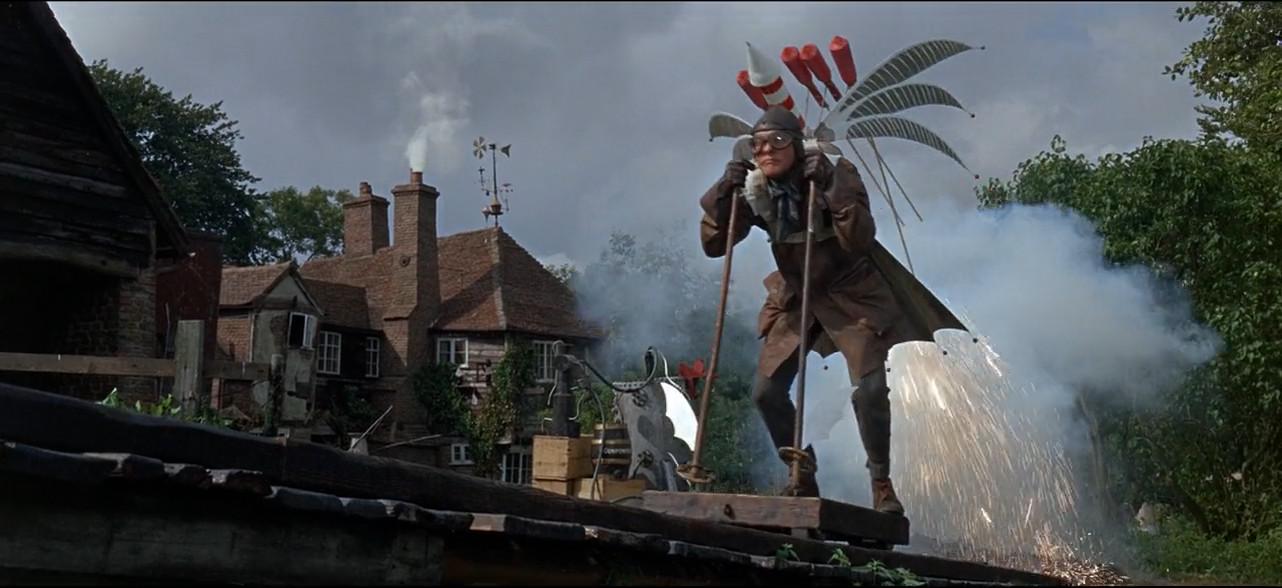A man in a leather aviator coat, cap and goggles, with homemade wings and a cluster of fireworks strapped to his back, sprints down a wooden launch ramp on a rooftop as the rockets spray sparks and smoke behind him.
